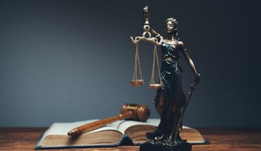 Apelação criminal: Estátua da deusa da justiça com balança e espada, com martelo de juiz e livro ao fundo.